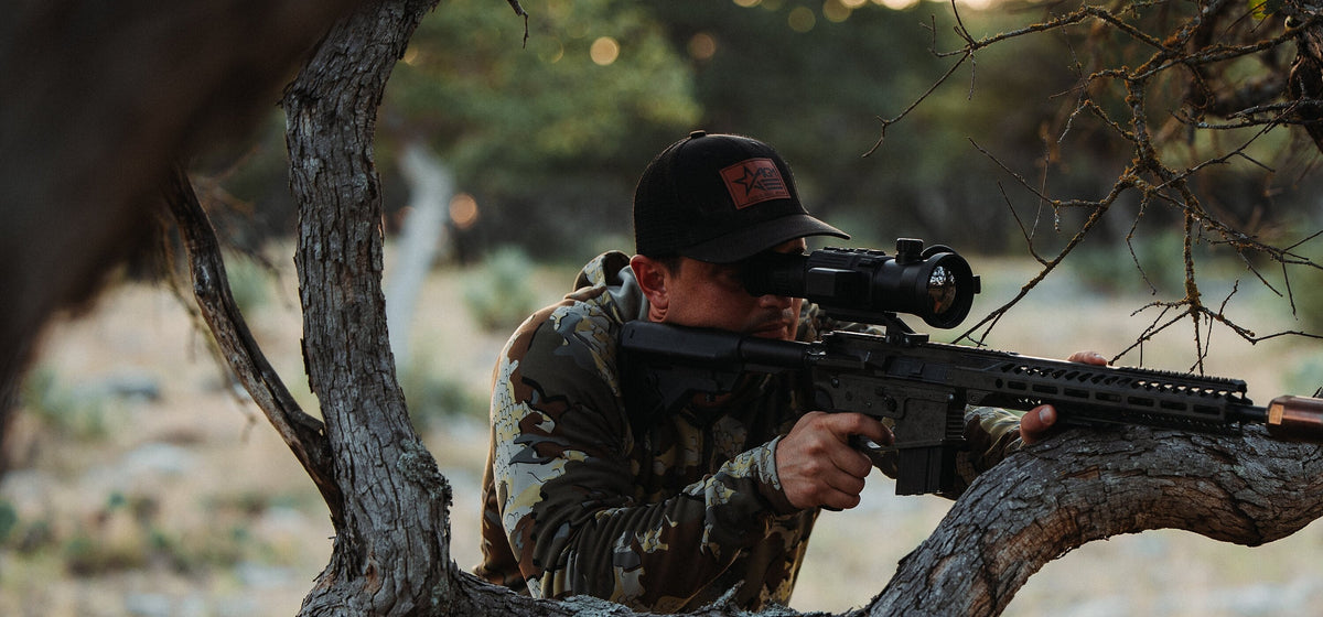 Hunter aiming an AGM thermal riflescope from a tree